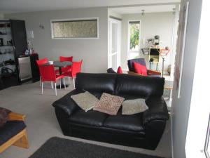 uma sala de estar com um sofá de couro preto e cadeiras vermelhas em Beach side Apartment Nelson em Nelson