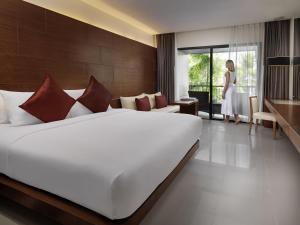 a bedroom with a large white bed and a woman standing in a room at Novotel Phuket Kata Avista Resort and Spa in Kata Beach +257 photos