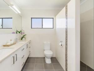 a white bathroom with a toilet and two sinks at The Lazy Tide in Burrum Heads