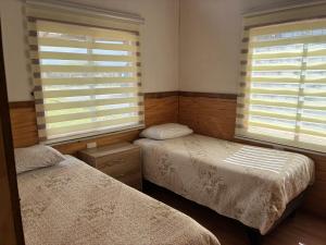 a bedroom with two beds and two windows at Cabaña El Rincón de las Flores in Chaitén