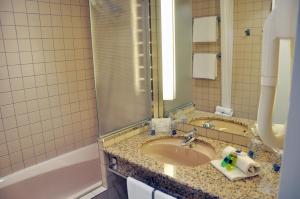 une salle de bain avec un lavabo, une baignoire et un miroir dans l'établissement Novotel Andorra, à Andorre-la-Vieille