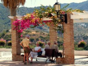 a group of people sitting on a bench under an arch with flowers at Apartamentos Balcón de Maro in Maro