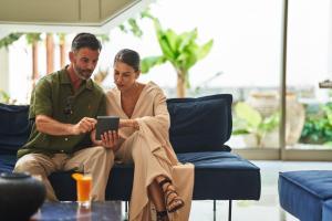 a man and woman sitting on a couch looking at a tablet at Agapi Beach Resort Premium All Inclusive in Amoudara Herakliou