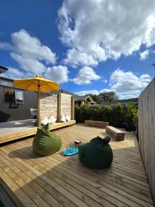 een houten terras met twee grote groene zitstoelen en een parasol bij Puriri Tiny Home in Orewa