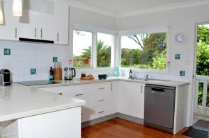 eine weiße Küche mit weißen Schränken und Fenstern in der Unterkunft Classic Meets Contemporary 1960's Beach House in Malua Bay