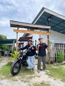 zwei Männer stehen neben einem Motorrad vor einem Haus in der Unterkunft Soyak Senja Roomstay in Langkawi Intl