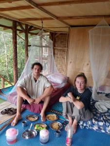 two people sitting in a tent with plates of food at WOOD CABIN LODGE IN THE FOREST book here treking with us in Bukit Lawang