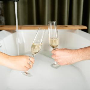 two people holding champagne glasses in front of a bath tub at Hotel Ari Gjakove in Gjakove