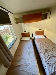 deux lits dans une petite pièce avec une fenêtre dans l'établissement La Yole Mobilhome Premium 6 pers avec terrasse lounge, à Vendres