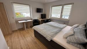 a bedroom with a bed and a desk and two windows at Gästehaus Fries in Blankenheim