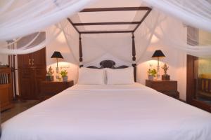 une chambre avec un grand lit avec des draps et des oreillers blancs dans l'établissement Dhyana Beach Villa, à Ambalangoda