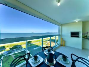 a dining room with a table and chairs and a large window at Apto Frente Mar Bali Beach Home Club 3 Quartos Climatizados Cozinha Completa Sacada com Churrasqueira 2 Vagas de Garagem Piscina borda infinita Sauna Academia Cinema Quadra Salão de Jogos Pé na Areia 15min do Beto Carrero in Piçarras