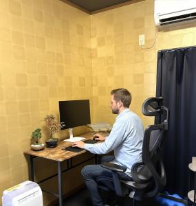 Ein Mann, der an einem Schreibtisch mit einem Computer sitzt. in der Unterkunft ミラージュ宿 2025年5月オープン 京都芸術 1軒家貸切 in Kyoto