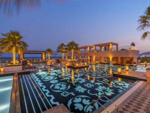 a resort with a pool with palm trees and a building at Fairmont Fujairah Beach Resort in Al Aqah