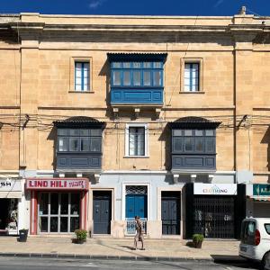 a man walking in front of a building with blue windows at Charming 1-bed place in historic, vibrant Hamrun near Valletta in Hamrun