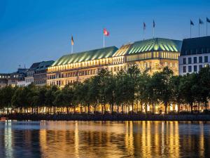 a building with flags on top of it next to a river at Fairmont Hotel Vier Jahreszeiten in Hamburg