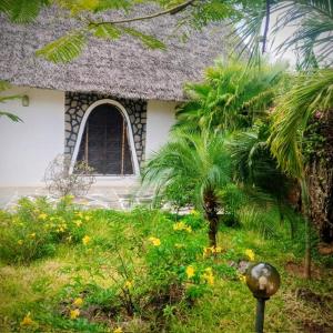 a house with a thatched roof and a garden with flowers at Casa Madro in Malindi