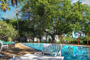 a swimming pool with two white chairs and trees at Jade Green Hotel Hambantota in Hambantota