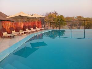 a swimming pool with chairs and an umbrella at Uukwaluudhi Safari Lodge in Okahao