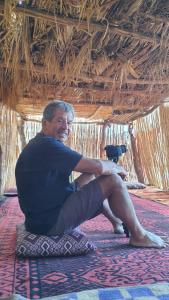 ein Mann, der mit einer Kamera auf einem Teppich sitzt in der Unterkunft Camp Golden Desert Morocco in Mhamid