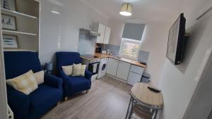 a living room with two blue chairs and a kitchen at Cove Bay 1 Bed Flat in Largs