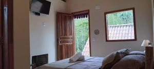 a bedroom with a bed and a window and a television at Chalé Cogumelo Refugio dos Gnomos in Visconde De Maua