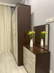 a dresser with a mirror and vases with yellow flowers on it at Новая уютная комфортная квартира с современным ремонтом in Astana +2 photos