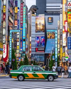 a green car driving down a busy city street at Shinjuku Downtown新宿 in Tokyo