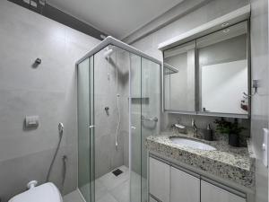 a bathroom with a glass shower and a sink at Ap Pitangueiras - 3 suítes - Pé na Areia - Ao lado do Shopping in Guarujá