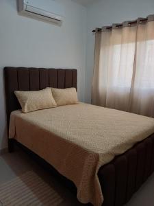 a bed with a brown headboard and a window at Sunrise Apartments in San Felipe de Puerto Plata