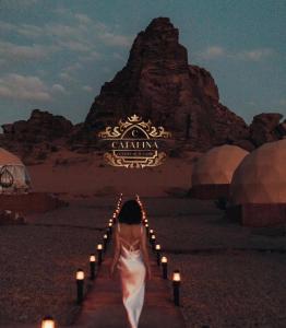a woman in a white dress walking down a path with candles at Catalina Luxury rum camp in Wadi Rum