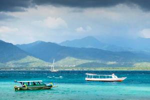 two boats in the water with mountains in the background at Cleosa 2 BR Cozy Bungalow Family ZN301 in Gili Air +8 photos