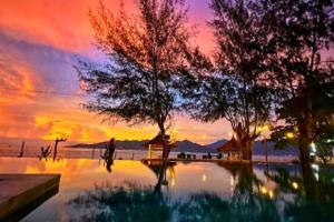 a sunset over a swimming pool with trees in the foreground at Cleosa 2 BR Cozy Bungalow Family ZN301 in Gili Air