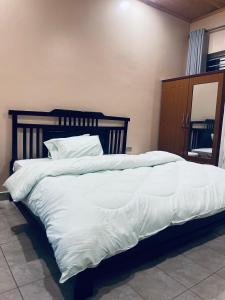 1 cama grande con sábanas blancas y cabecero de madera en Émeraude Kigali, en Kigali