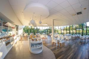 a restaurant with white tables and chairs and windows at Mercure Poitiers Site du Futuroscope in Chasseneuil-du-Poitou