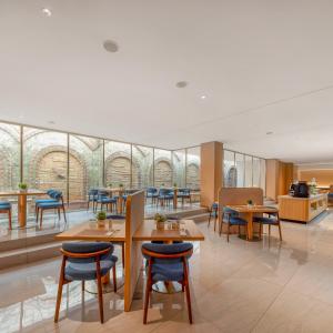 a restaurant with tables and chairs and windows at Model J Hotel Jakarta Central Park 曼居酒店 雅加达中央公园店 in Jakarta