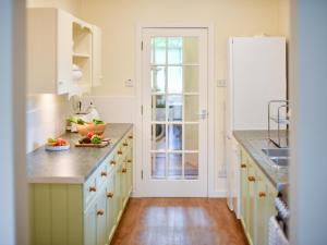 a kitchen with white cabinets and a wooden floor at Pinclanty Cottage in Pinmore