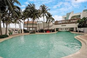 a swimming pool in front of a building with palm trees at Southeast Oceanfront Residence in Hollywood Beach