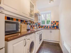 a kitchen with white cabinets and a washer and dryer at Horseshoe Cottage-Uk37360 in Lympsham +11 photos