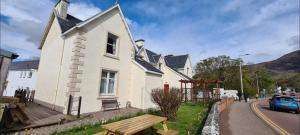 a white house with a bench next to a street at Nevis Bank Studio in Fort William