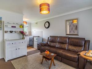 a living room with a brown leather couch and a kitchen at The Little House in Kessingland