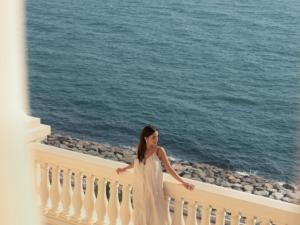 a woman in a white dress standing on a balcony overlooking the ocean at Raffles The Palm in Dubai +220 photos