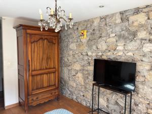 a stone wall with a television and a chandelier at Chambre suite de L'argentier in Noyarey