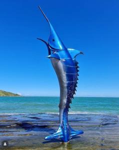 a blue statue of a fish on the beach at Perto do peixe Marley - Praia do Morro in Guarapari