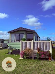 a green tiny house with a fence and flowers at Dune View Caravan in Ynys-lâs Station