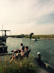 drie mensen zitten aan de rand van een wateroppervlak bij Tiny Boat House #4 in Garnwerd