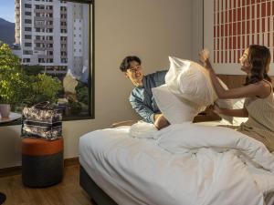 a man and woman sitting on a bed playing with pillows at ibis Chiang Mai Nimman Journeyhub in Chiang Mai