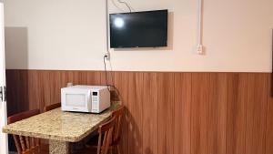 a microwave on a table with a tv on a wall at Mares e Flores de Bombinhas in Bombinhas