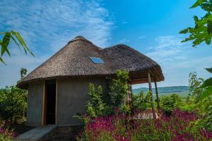 a small hut with a thatched roof and purple flowers at Nzoghu Heritage Safari Camp in Kasese +9 photos