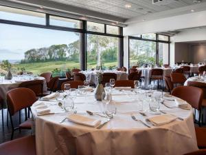 une salle à manger avec tables, chaises et fenêtres dans l'établissement Mercure Bayeux Omaha Beach, à Port-en-Bessin-Huppain